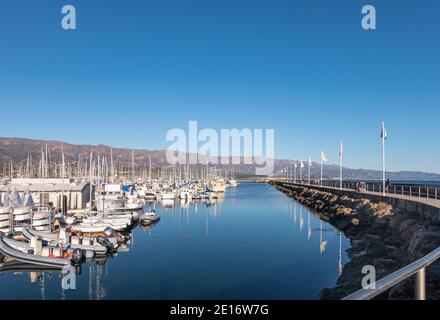 USA, California, Santa Barbara - 18 dicembre 2020: Porto yacht. Molte barche con l'uscita di acqua blu lungo il porto roccioso passeggiata diga frangiflutti sotto blu Foto Stock