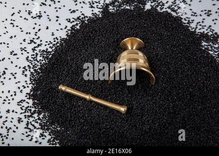 Semi di Nigella sativa noti anche come cumino nero, kalo jeera, kalonji e caraway nero in paletta di ferro e mortaio su sfondo bianco di legno con copy sp Foto Stock