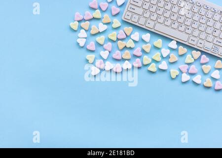 Caramelle a forma di cuore e tastiera computer su un tavolo blu. Concetto di San Valentino. Vista dall'alto, disposizione piatta, spazio per la copia. Foto Stock