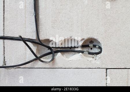 Fori in una parete di blocchi di cemento con fili per prese di corrente, nel processo di costruzione di una casa Foto Stock