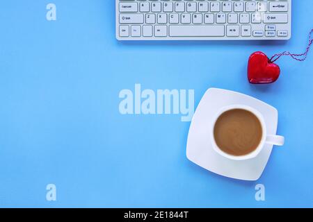Tastiera, una tazza di caffè e un cuore rosso giocattolo su sfondo blu. Concetto di giorno di San Valentino. Vista dall'alto, disposizione piatta, spazio per la copia. Foto Stock