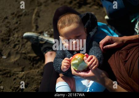 Una giovane madre sta offrendo al suo bambino una mela sopra la spiaggia in autunno Foto Stock