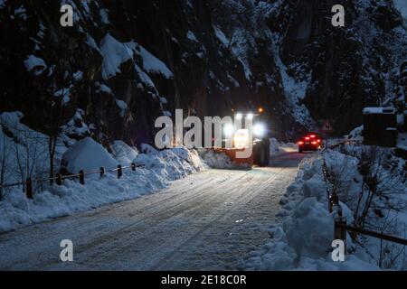 lo spazzaneve passa con le luci attraverso le strade di montagna innevate di sera per ripulire il traffico stradale Foto Stock