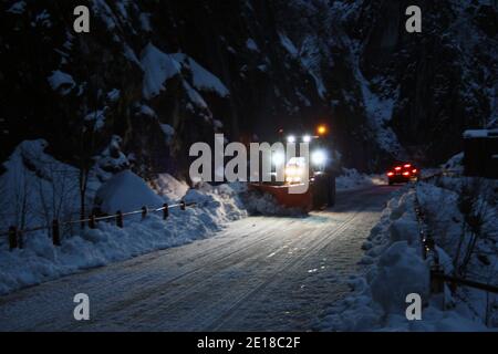 lo spazzaneve passa con le luci attraverso le strade di montagna innevate di sera per ripulire il traffico stradale Foto Stock