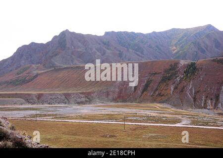 Una strada di campo che corre lungo le colonne nelle pianure vicino alle terrazze circondate da alte montagne. Altai, Siberia, Russia. Foto Stock