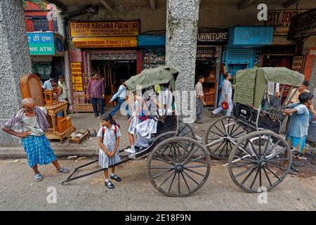 14-ago-2007 tirato Rickshaw o Ricksha un trasporto umano-alimentato come bus della scuola parcheggiato sul marciapiede, Kolkata, India. Foto Stock