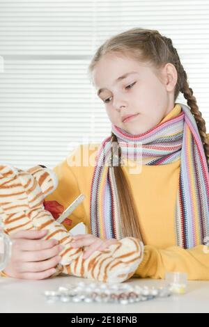 Malata con toy tiger seduta a tavola con la medicina a casa Foto Stock