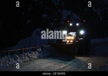 lo spazzaneve passa con le luci attraverso le strade di montagna innevate di sera per ripulire il traffico stradale Foto Stock