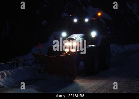 lo spazzaneve passa con le luci attraverso le strade di montagna innevate di sera per ripulire il traffico stradale Foto Stock