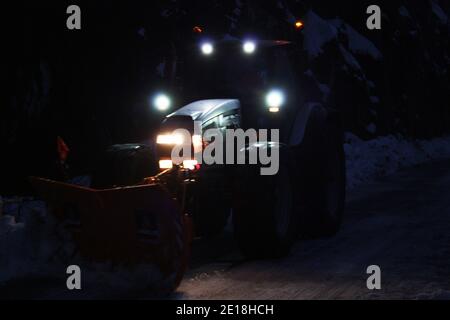 lo spazzaneve passa con le luci attraverso le strade di montagna innevate di sera per ripulire il traffico stradale Foto Stock