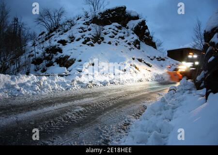 lo spazzaneve passa con le luci attraverso le strade di montagna innevate di sera per ripulire il traffico stradale Foto Stock