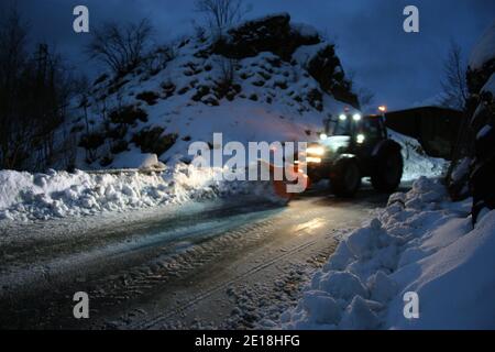 lo spazzaneve passa con le luci attraverso le strade di montagna innevate di sera per ripulire il traffico stradale Foto Stock