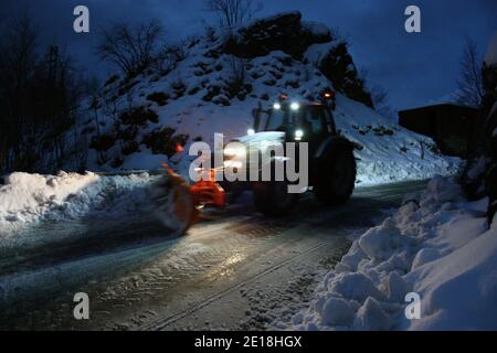 lo spazzaneve passa con le luci attraverso le strade di montagna innevate di sera per ripulire il traffico stradale Foto Stock