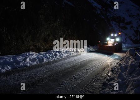 lo spazzaneve passa con le luci attraverso le strade di montagna innevate di sera per ripulire il traffico stradale Foto Stock