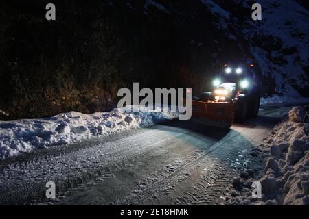 lo spazzaneve passa con le luci attraverso le strade di montagna innevate di sera per ripulire il traffico stradale Foto Stock