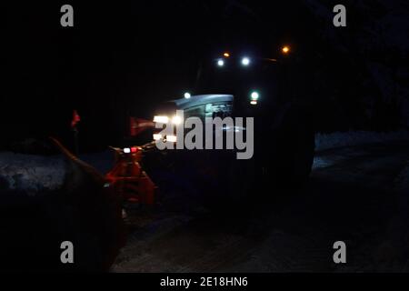 lo spazzaneve passa con le luci attraverso le strade di montagna innevate di sera per ripulire il traffico stradale Foto Stock