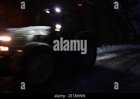 lo spazzaneve passa con le luci attraverso le strade di montagna innevate di sera per ripulire il traffico stradale Foto Stock