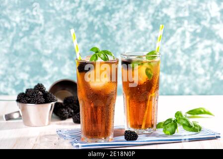 Il bicchiere di tè freddo con mora su tavolo di legno. Cuba Libre o cocktail a lunga isola, bevanda fredda o limonata con limone e basilico. Verde turchese Foto Stock