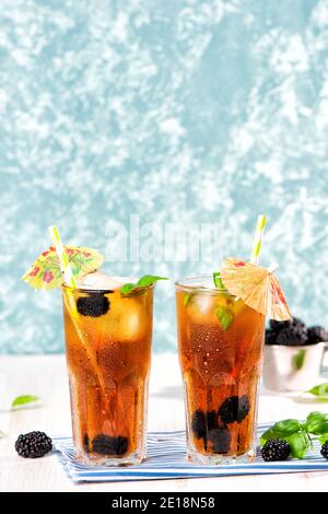 Il bicchiere di tè freddo con mora su tavolo di legno. Cuba Libre o cocktail a lunga isola, bevanda fredda o limonata con limone e basilico. Verde turchese Foto Stock