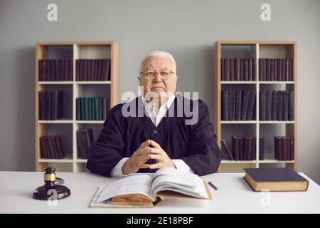 Saggio giudice maturo seduto alla scrivania con codice aperto di Legge nel suo ufficio o in aula Foto Stock