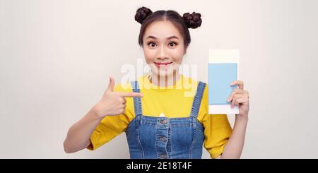 Giovane bella donna turistica asiatica in vacanza tenendo passaporto puntando con le dita, simbolo eccellente Foto Stock