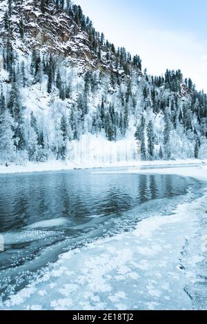 Riva ghiacciata del lago con foresta innevata. Clima freddo, letto del fiume ghiacciato a causa di un brusco scatto freddo Foto Stock