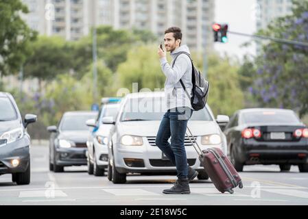 Giovane uomo con bagagli che attraversano la strada Foto Stock