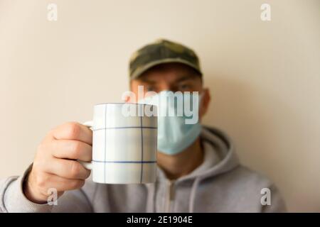Un uomo in una maschera chirurgica che tiene una tazza Foto Stock