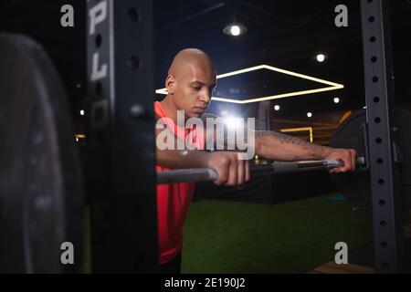 Uomo africano atletico forte sicuro che si prepara per gli squts barbell esercizio in palestra, copia spazio. Bel sportivo che si concentra prima di sollevare wei Foto Stock