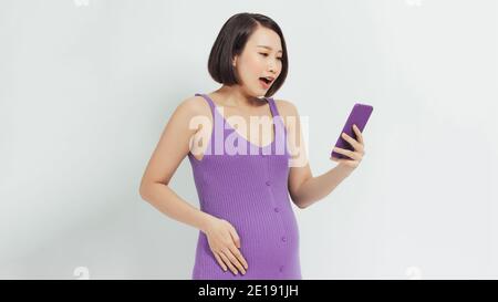 Donna incinta stupita che guarda contenuti multimediali in uno smartphone Foto Stock