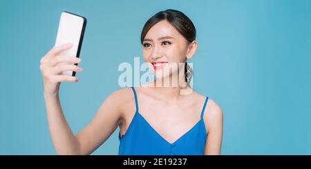 Felice attraente ragazza asiatica prendendo un seldie isolato blu su sfondo pastello Foto Stock