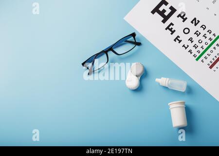 Controlli e prevenzione della visione, occhiali, lenti e gocce per la correzione della visione su sfondo blu, vista dall'alto. Accessori per oftalmologo. Foto Stock