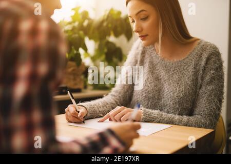 Bella bionda giovane studentessa studia e scrive in biblioteca con un amico. Foto Stock