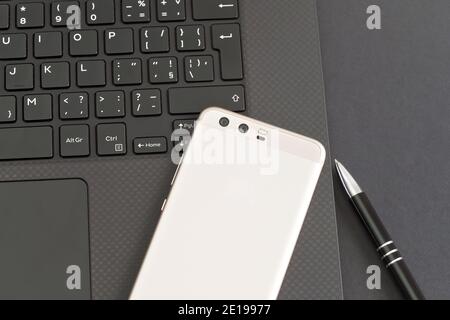 Tastiera nera per computer portatile, telefono cellulare e penna sul tavolo grigio - vista dall'alto Foto Stock