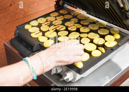 Patate tagliate a piccoli pezzi grigliate sulla griglia elettrica, mano più alta sfocata su di loro mentre si stanno muovendo sopra Foto Stock