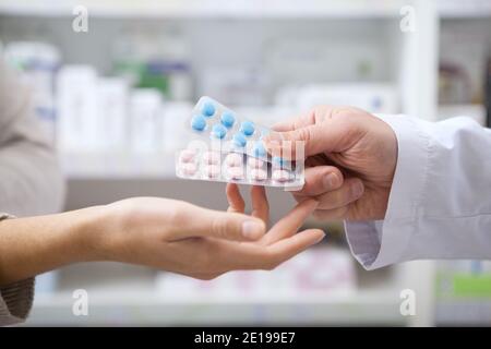 Primo piano corto di un farmacista professionale che consegna blister con pillole alla sua cliente femminile. Donna che acquista farmaci alla farmacia, recei Foto Stock