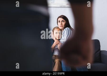 Donna spaventata abbracciando figlia vicino marito abusivo su primo piano offuscato a casa Foto Stock