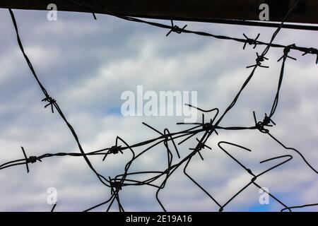 Filo spinato di metallo contro un cielo blu coperto in primavera o in inverno e un buco nella recinzione. Proteggere un parcheggio, un business o un carcere. Foto Stock