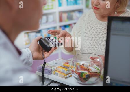 Un colpo corto di una donna anziana che paga con carta di credito alla farmacia. Anziana cliente femminile che paga per il suo farmaco, inserendo il pin di sicurezza in rosso Foto Stock