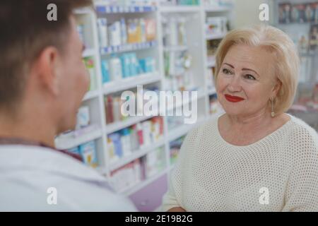 Donna anziana sorridente allegra, parlando con il farmacista, shopping per la medicina alla farmacia locale. Anziana cliente donna che acquista farmaci presso il Foto Stock