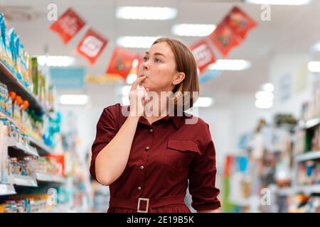 Consumismo. Ritratto di una giovane donna che sceglie con attenzione i prodotti in un supermercato. Concetto di shopping. Foto Stock