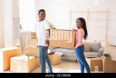 Coppia nera amorevole che trasporta scatola di cartone insieme, aiutandosi l'un l'altro nella loro nuova sede durante il giorno in movimento Foto Stock