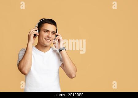 Relax, buon umore e musica. Un giovane studente felice e attraente indossa le moderne cuffie wireless Foto Stock