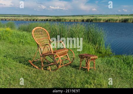 Sedia a dondolo in vimini vuota in piedi accanto al piccolo sgabello in vimini, su un fiume Sura in attesa di qualsiasi uomo per rilassarsi Foto Stock