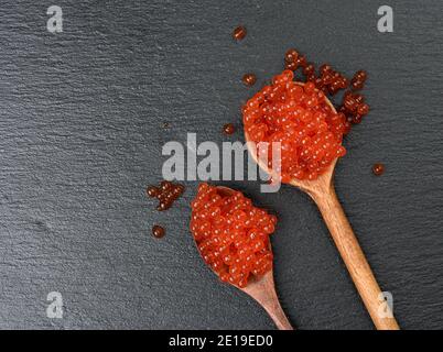 caviale fresco di salmone al chum rosso granato in cucchiaio di legno, sfondo nero, vista dall'alto Foto Stock