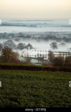 Paesaggio di campagna misty con strati di nebbia in una valle con colline, campi verdi e terreni agricoli con una splendida vista del paesaggio tipico inglese, il Cotswolds, Inghilterra, Regno Unito Foto Stock