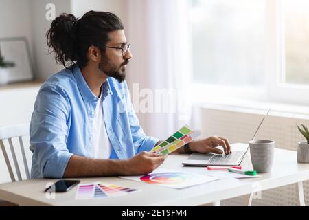Young Eastern Freelance Designer Guy lavorare con notebook e colore Campioni Foto Stock