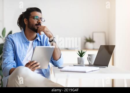 Giovane freelance arabo maschile che usa Gigital Tablet e Daydreaming A casa Foto Stock