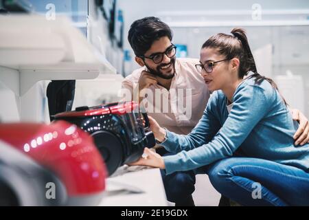 Giovane marito e moglie adorabili che decidono quale aspirapolvere acquistare nel negozio di elettronica. Foto Stock