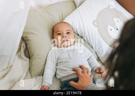 Bambino ragazzo sorridente carino in beige 5-6 mesi guardando macchina fotografica con madre sul letto con coperta a maglia Foto Stock